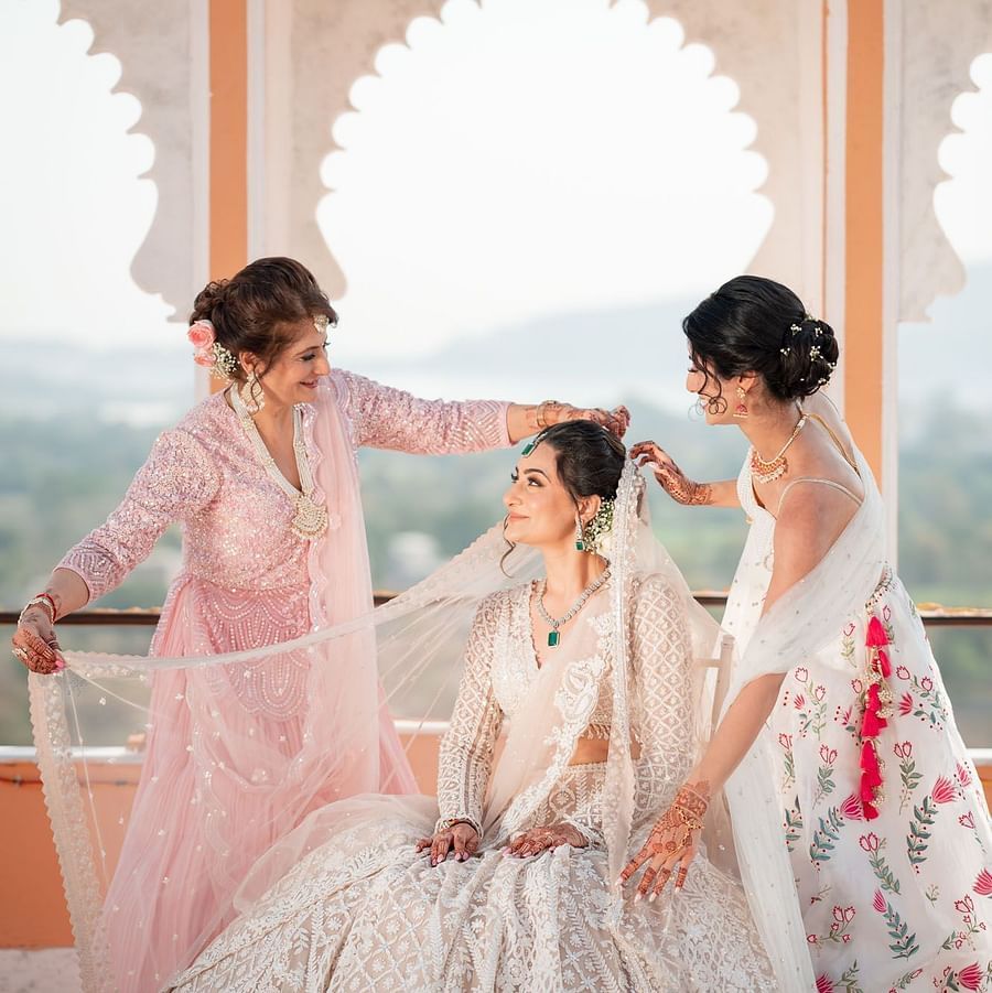 Two girls stand on either side of the bride, adjusting her dupatta at Fateh Vilas Collection Udaipur