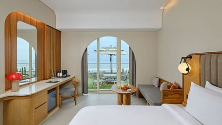 Image of Premium Room at Swosti Premium Beach Resort in Puri featuring a plush bed and a couch with a coffee table next to the doorway to the outdoor sitting space with the majestic view of the sea