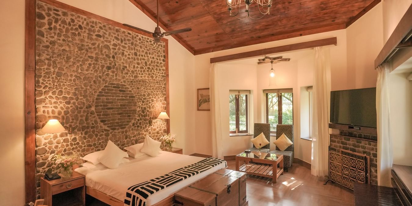 A bedroom with a bed, a patterned rug, and warm lighting, wooden interior - The Den Corbett Resort & Spa, Kumeria.