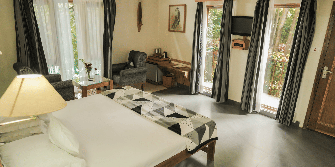 A living room with a couch, chairs, and a view of a garden - The Den Corbett Resort & Spa, Kumeria.