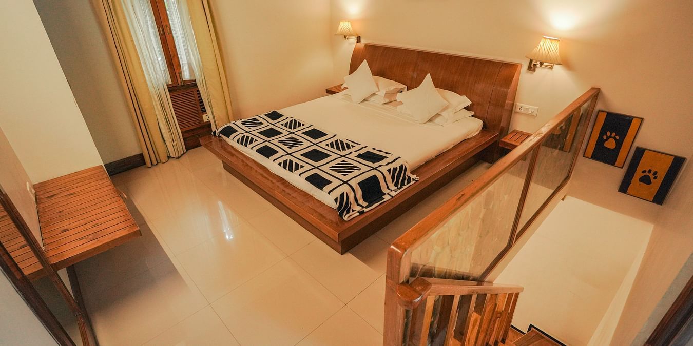 A bedroom with a bed, a chair, and a patterned rug, warm lighting - The Den Corbett Resort & Spa, Kumeria.