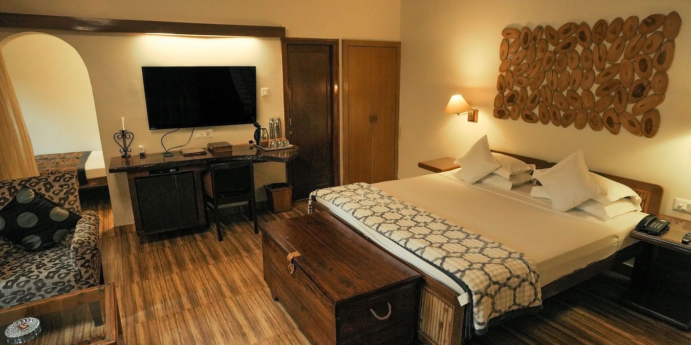 A bedroom with a bed, a television, and warm lighting, wooden interior - The Den Corbett Resort & Spa, Kumeria.