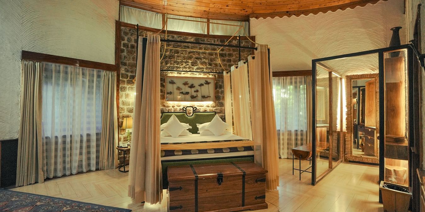 A bedroom with a wooden bed frame, a patterned rug, and warm lighting - The Den Corbett Resort & Spa, Kumeria.