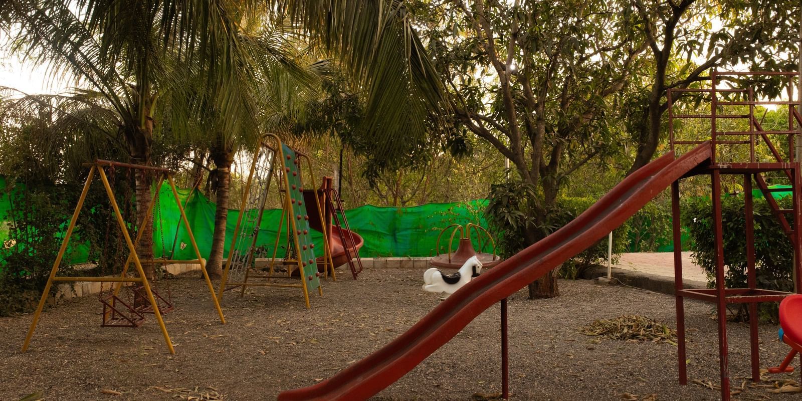 An outdoor children's play area with green swings and a red slide at Daksh Resort & Amusement Park, Sasan Gir.