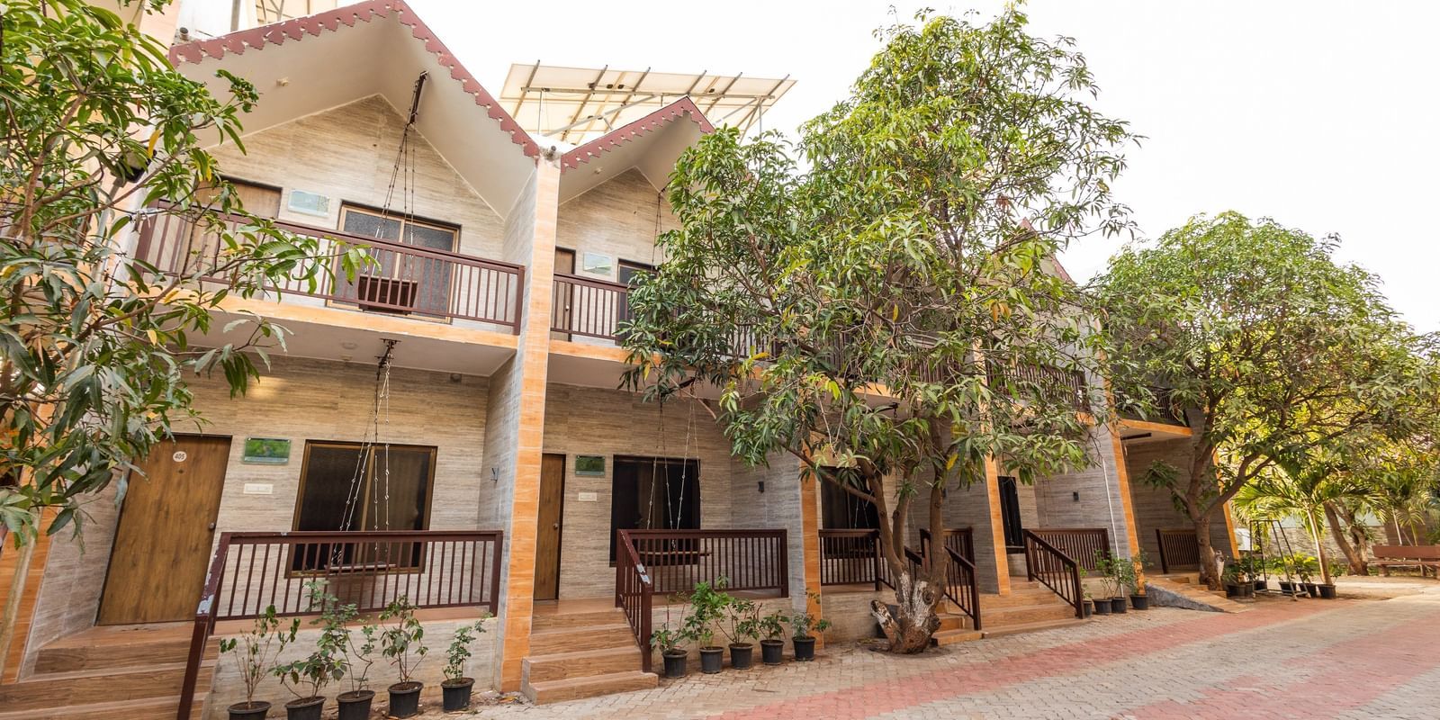 Exterior view of Daksh Resort & Amusement Part featuring a two-storey resort building with balconies, trees, and a paved driveway in the front.