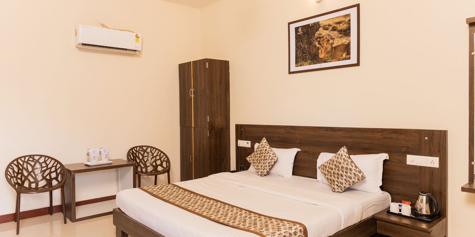 A double bed with patterned cushions, wall art, and chairs in a guest room at Daksh Resort & Amusement Park.