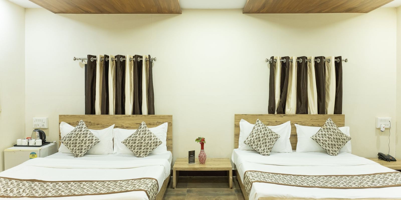 A guest room with two double beds, brown and white curtains, and ceiling lights at Daksh Resort & Amusement Park.