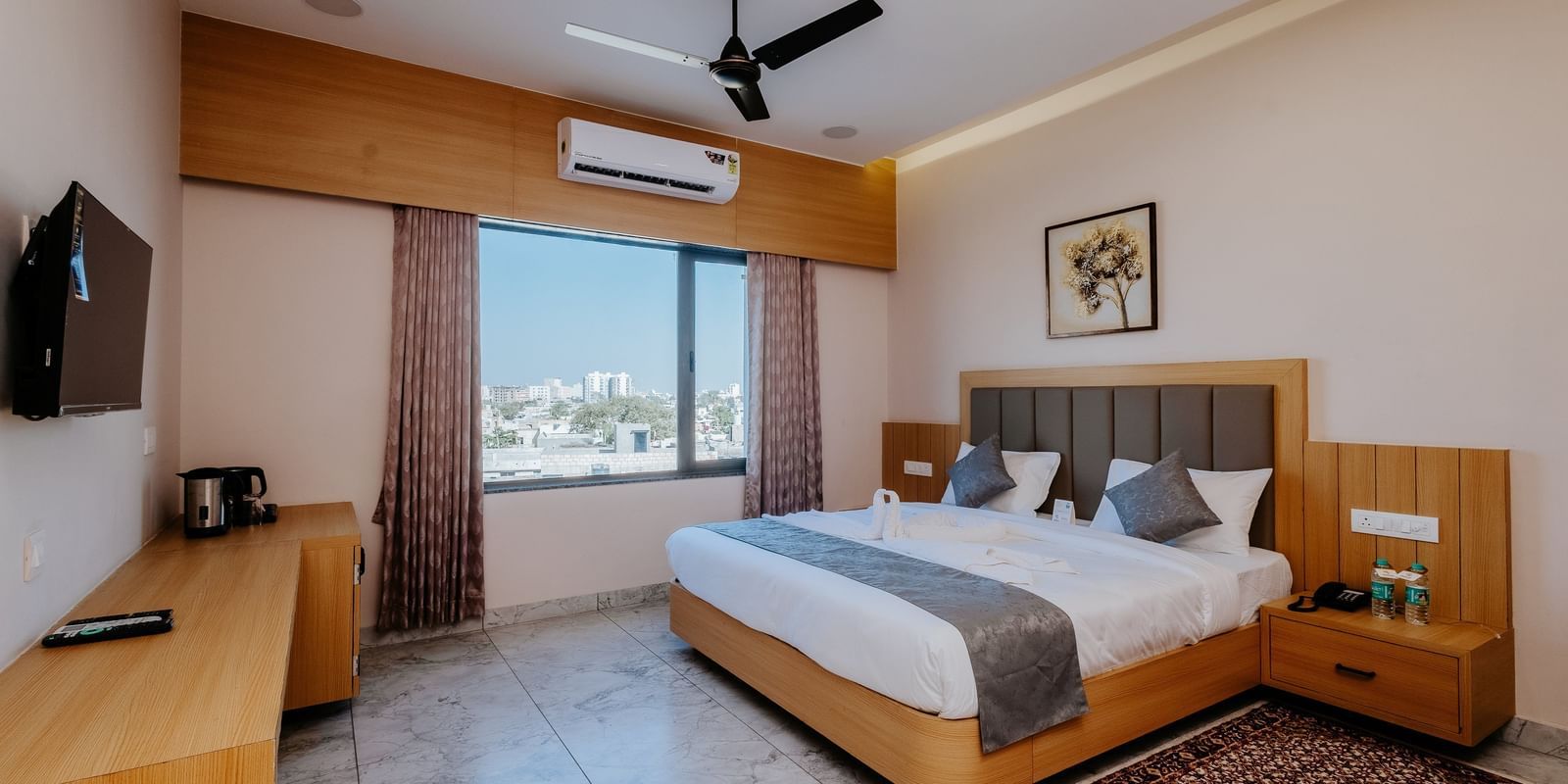 A well-appointed bedroom at Daksh The Grand Gowardhan, Dwarka, featuring a comfortable double bed, television, and window featuring views of the city.