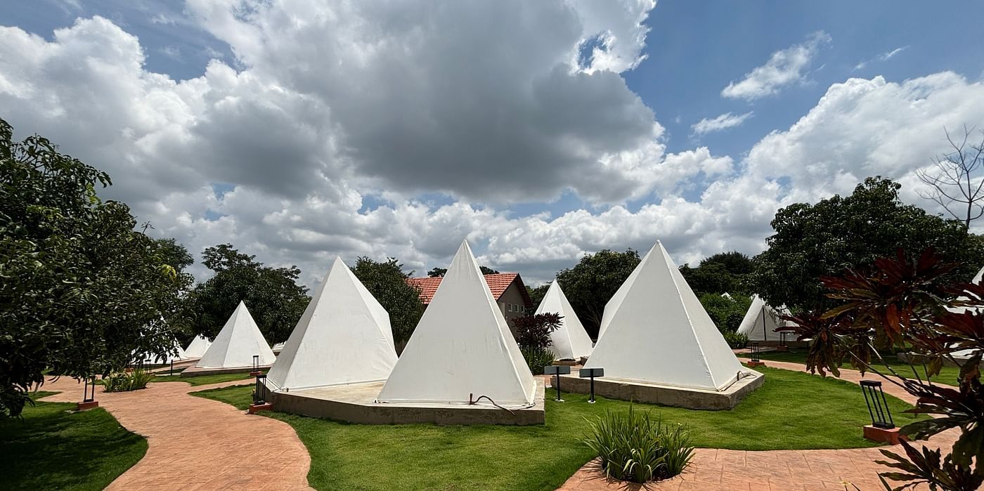 A scenic view of a resort area with tents lined along a neat walkway, surrounded by a well-maintained lawn.