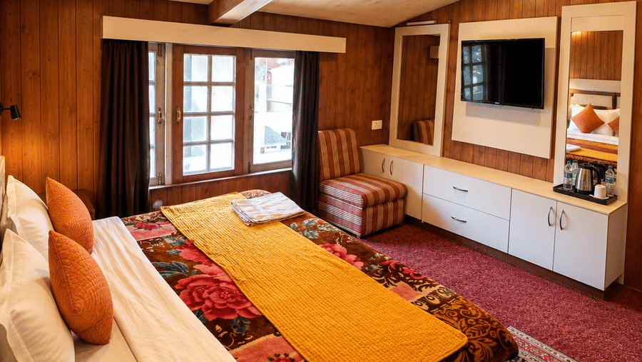 A bedroom at Hotel Outlook, Pahalgam, with a double bed, wood-panelled walls, a television console unit, a window, and a patterned rug.