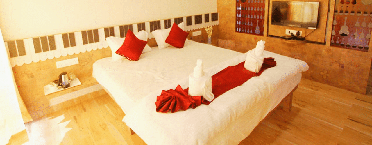 A diagonal view of the room featuring a spacious bed with towels folded in different shapes on it. There is a wooden table with a wall-mounted television at SeaFort Beach Resort