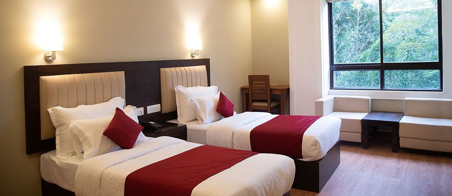 A hotel room in Gangtok featuring twin beds, warm lighting, and a window offering stunning views - Summit North Star, Gangtok