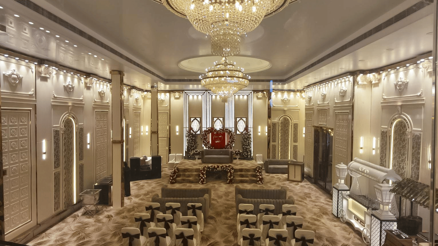 Extended view of the Aura banquet hall at Voyage Eastin Suite featuring a grand chandelier, chairs placed in theatre seating arrangement facing a podium with an upholstered chair.