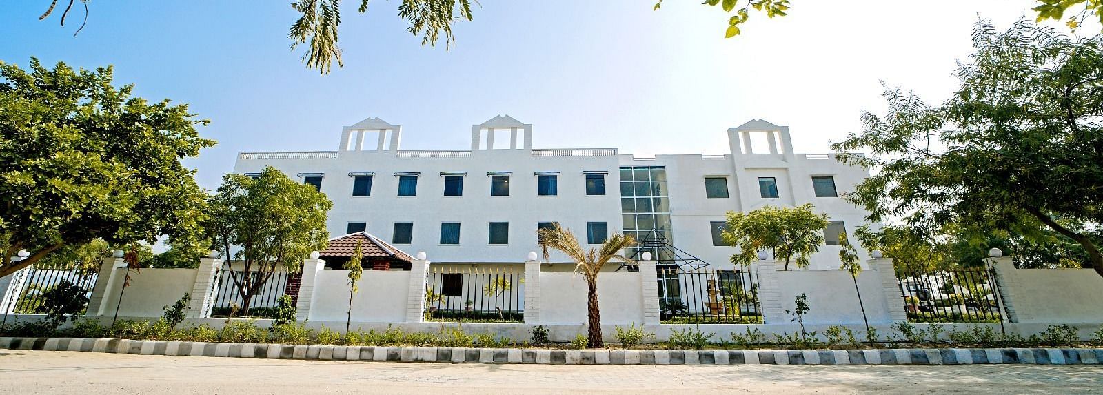 Front view of Grassfield Riveria Resort, Jaipur, surrounded by trees and clear skies, showcasing the modern building facade.