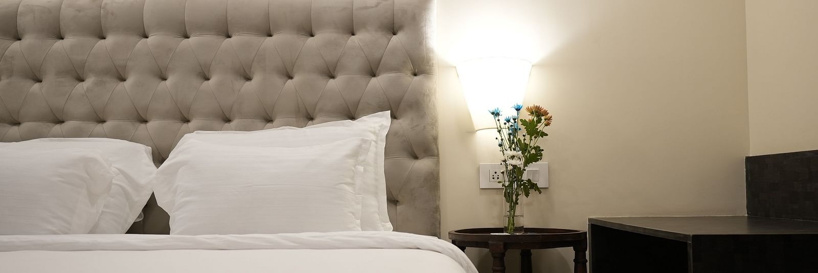 Close-up of a bed with plush pillows and a flower vase on the bedside table at The Verda de Miranda Resort.