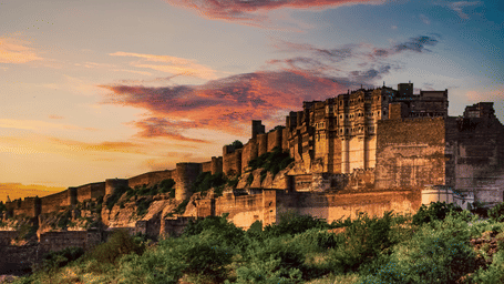 Ancient stone fort bathed in golden sunset light, with lush greenery in the foreground and colorful clouds in the sky.