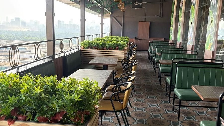 An outdoor seating area with tables and chairs is visible, featuring plants and a view of the surroundings - Melior Inn