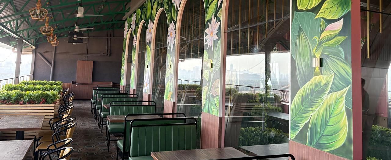 A dining area with green booth seating and large arched windows featuring decorative murals - Melior Inn