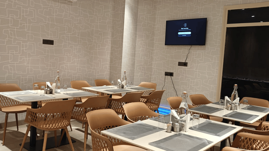 Modern indoor dining area at Hotel Bluestone Prime featuring neatly arranged tables with place settings, cushioned chairs, warm ambient lighting, and a clean contemporary design. The spacious layout offers a comfortable atmosphere suitable for relaxed meal