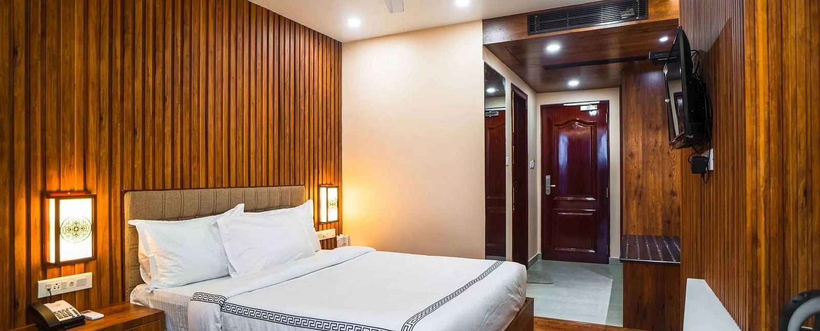 A cozy bedroom at Mansha Palace features wooden paneling, a comfortable bed, and a ceiling fan.