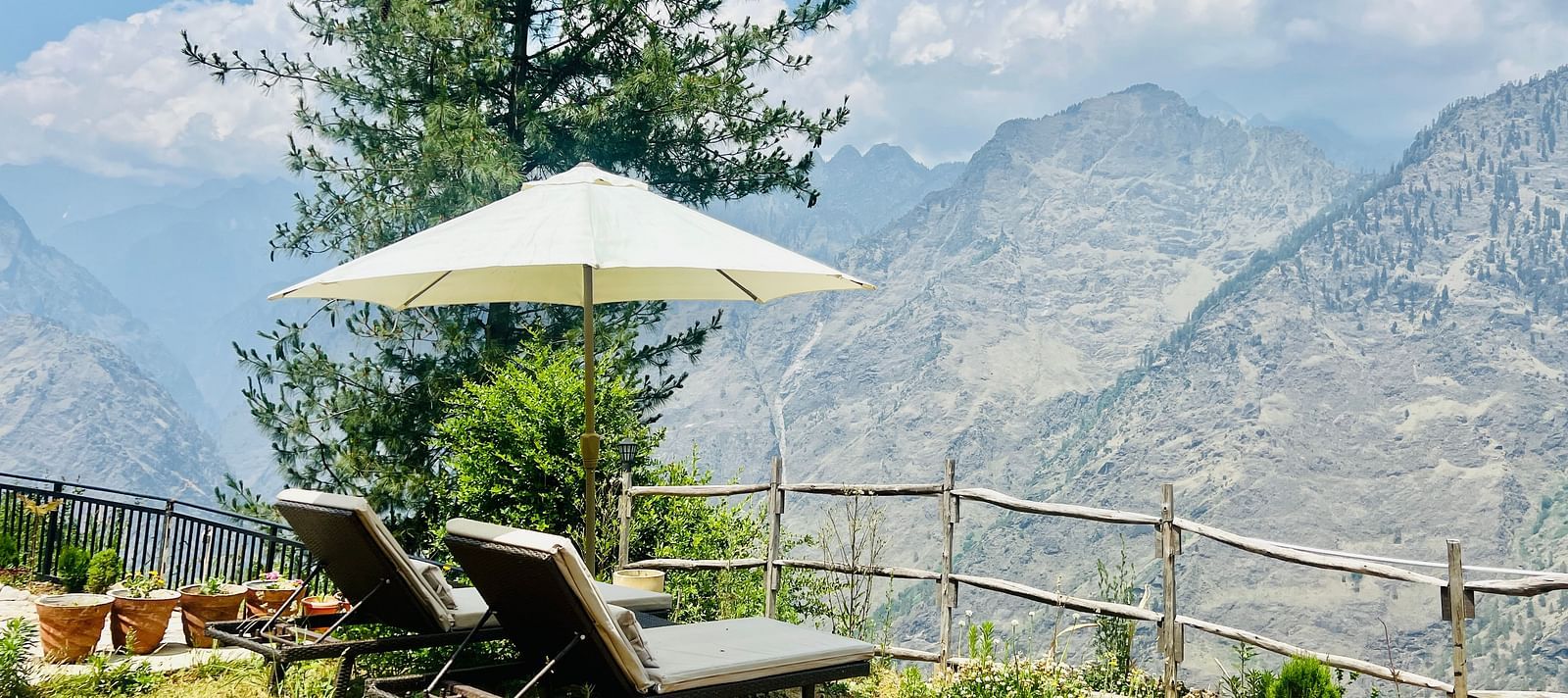 Relaxing outdoor lounge area with a white umbrella and sunbeds facing a mountain view  | Faraway Cottages, Auli