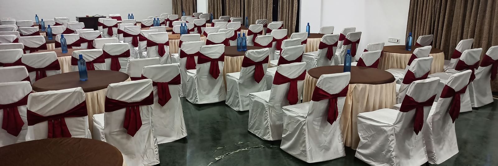 Cluster seating arrangement with white covers and maroon chair sashes, suitable for formal dining or events at Mayur Retreat.