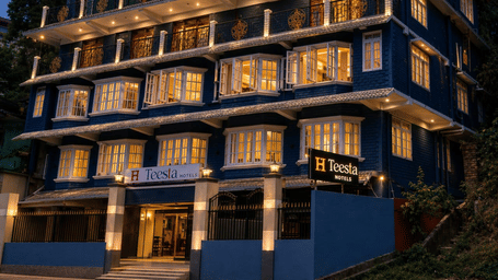 A hotel building with balconies and lights visible during evening at Teesta Hotel, Kalimpong.