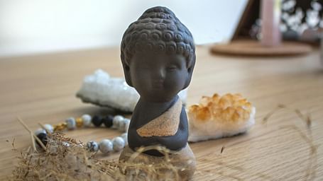 A Buddha sculpture placed on a wooden table along with a crystal bracelet, dry herbs, and crystals
