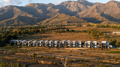 Aerial view of the multiple accommodations at Vandhara Sarovar Premiere, Jim Corbett - Patkote, set against a backdrop of mountains on a sunny day.