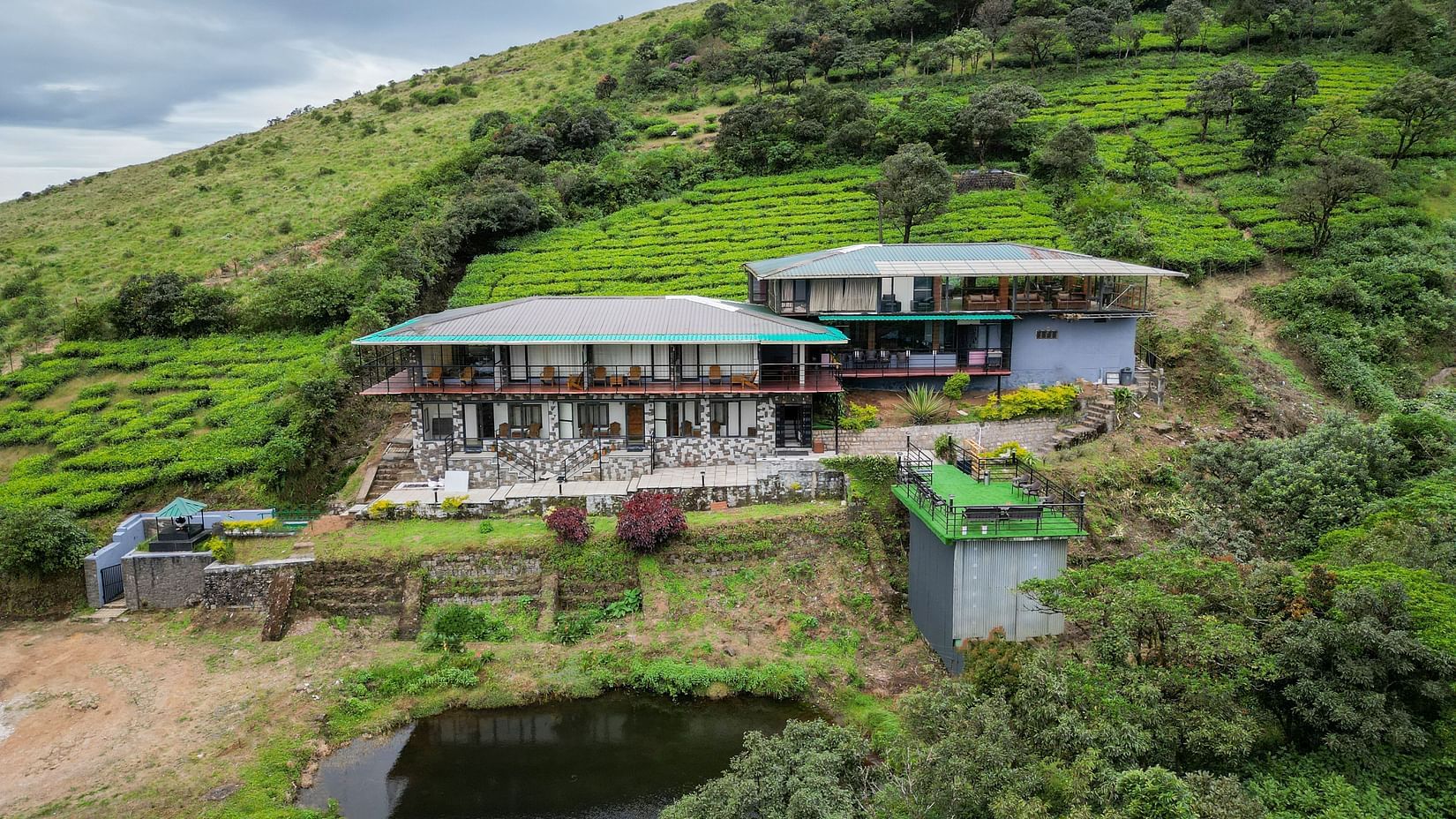 A wide angle shot of the resort on bright day with greenery all around and an artificial lake | Ibex Stays and Trails
