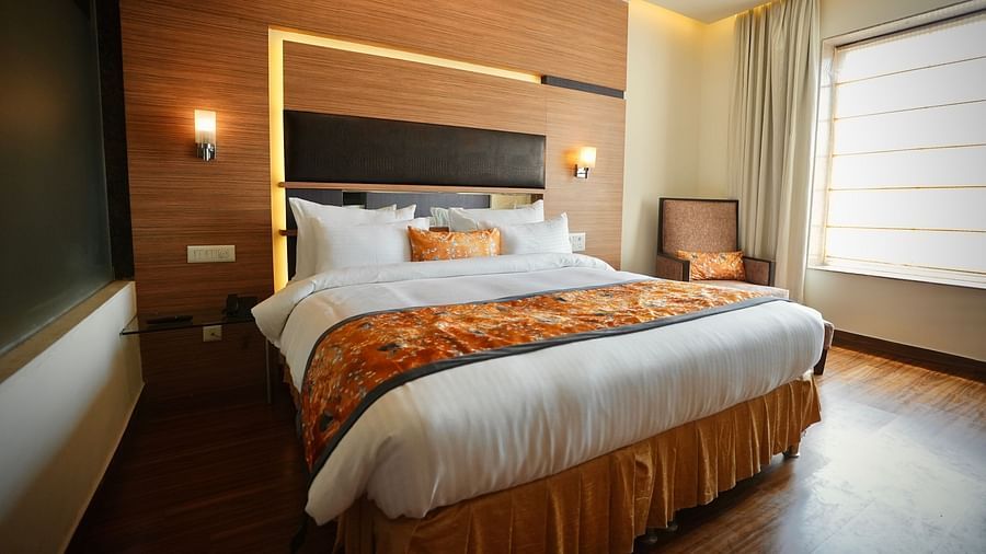 A bedroom featuring a bed with patterned bedding, a window with curtains, and a wooden wall panel - VITS Gurugram
