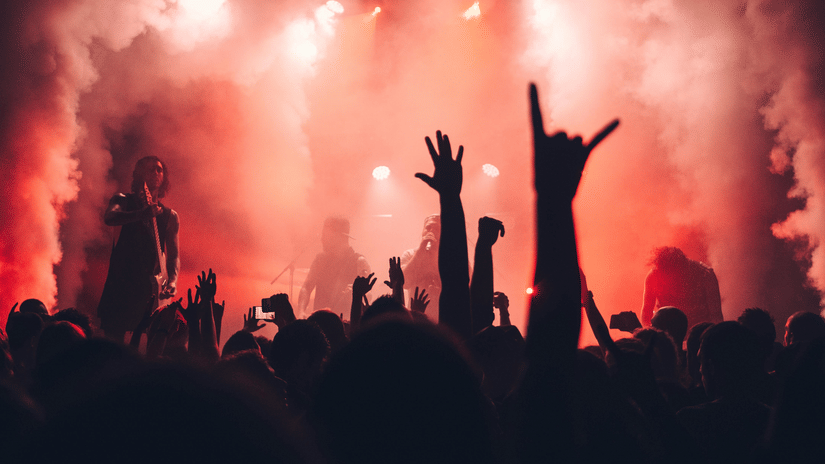 Crowd at a concert with hands raised in the air, lit by red stage lights and fog.