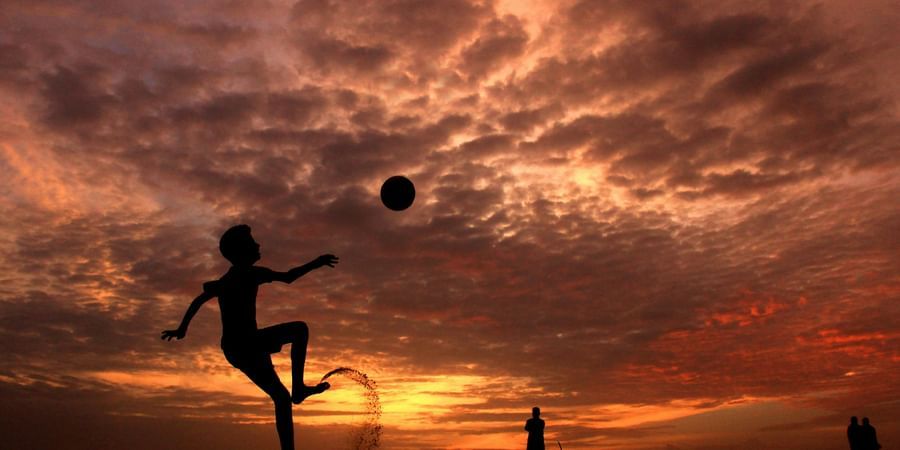 A silhouette of a person playing football at sunset with dramatic orange clouds in the sky.