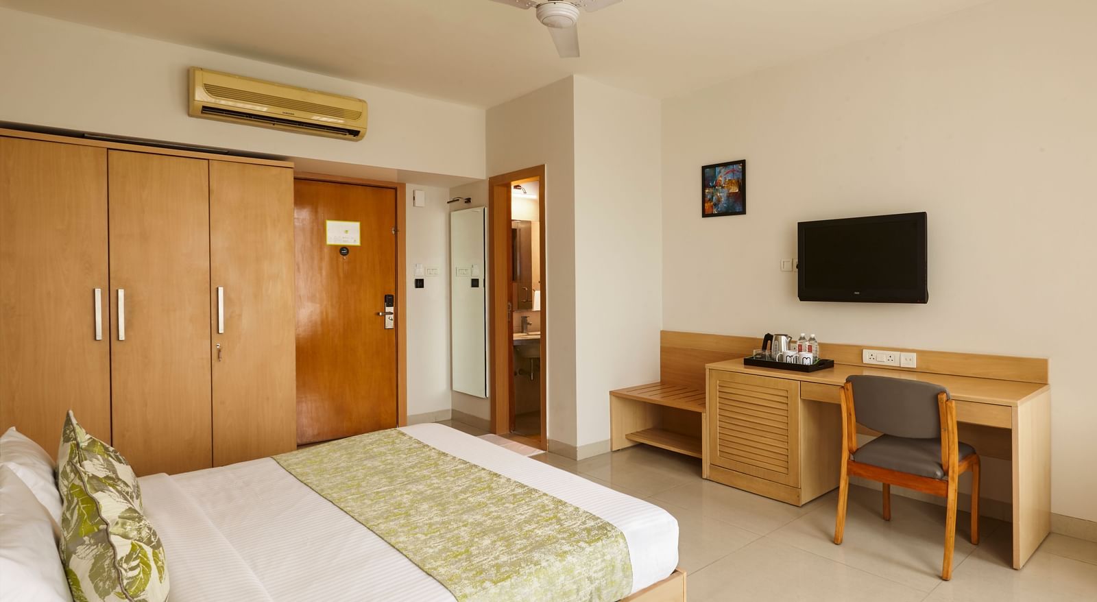A tidy hotel room at Monday Hotels Mahape, Navi Mumbai, featuring a large bed, TV, and a desk.