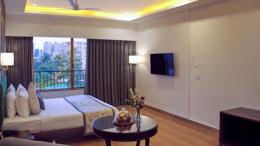 Bedroom with bed, wall-mounted TV, glass door with curtains, two chairs, and a round coffee table at Voyage Milestone Hotel and Banquet.