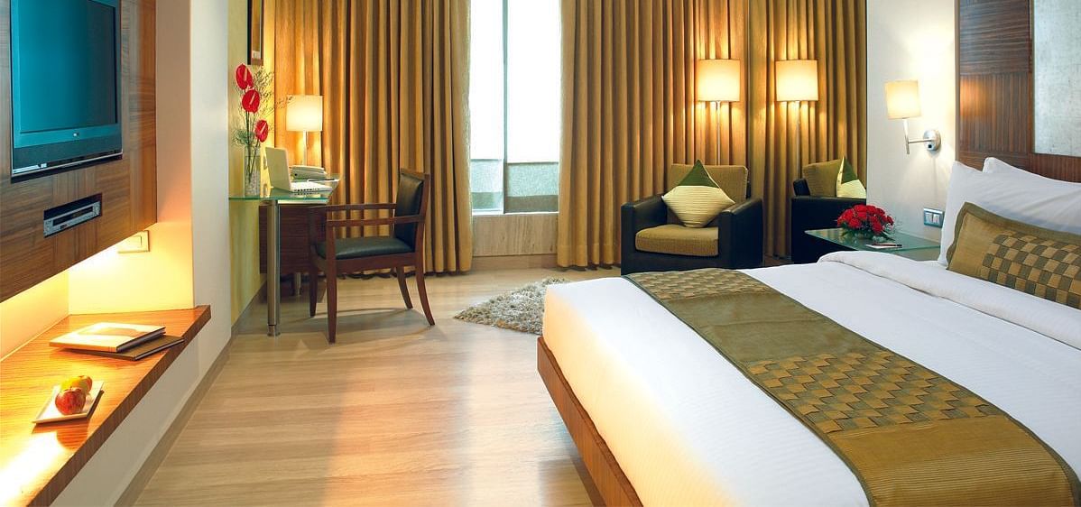 Image of a the executive room featuring a king size bed, a study table and chair, flat screen television, and an expansive window with golden curtains. | Mirage Hotel