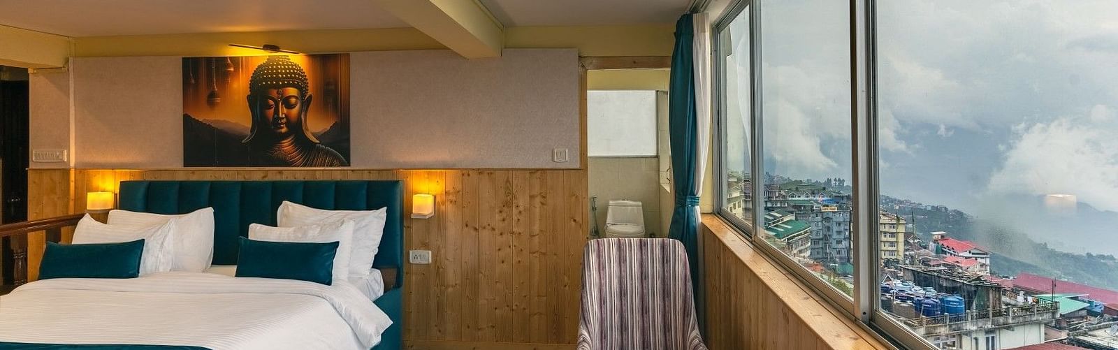Junior Suite at Avianna Seven Seas, Darjeeling with cosy twin beds, warm lighting, and large windows offering a panoramic view of Gangtok’s scenic hills and townscape.
