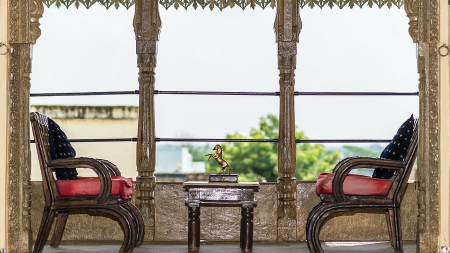 Two ornate chairs face a small table within a carved window frame at Fort Barli, creating a cosy and picturesque seating area.