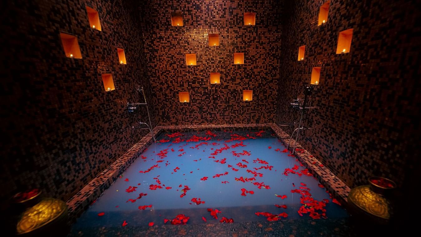 a bathtub with rose petals inside it and tea light candles kept on space in the wall - IOSIS Spa & Wellness