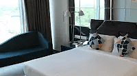 A neat bed with a plush comforter. A dark chair and a side table complete the room's layout.- Golden Suites, Gurgaon