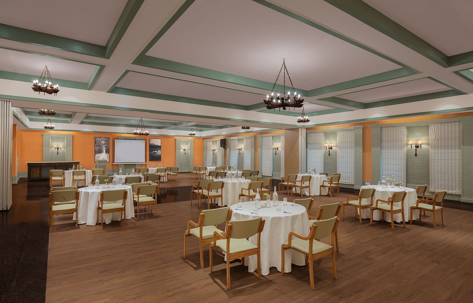 An image of a conference hall with a set of table and chairs in each corner and a projector screen at the front of the room - The Riverview Retreat, Corbett