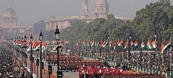 An aerial view captures the India Republic Day Parade on Kartavya Path (formerly Rajpath) in New Delhi, featuring marching contingents and spectators, with a large government building in the background. 