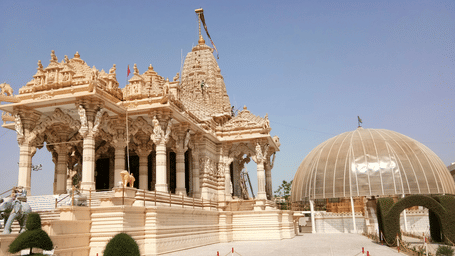 An overview of a Jain temple with a dome next to it and blue sky in the background. It is similar to the Kanch Mandir Indore.