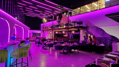A modern bar interior with purple and pink ambient lighting.
