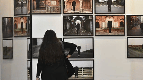 A person standing with back to camera inside a gallery space viewing displayed artwork, framed photographs on a wall, exhibition display.