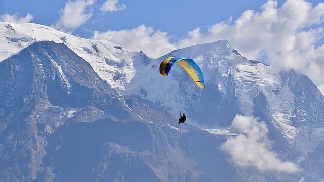 A person paragliding at a hill station with the backdrop of snow-capped mountains