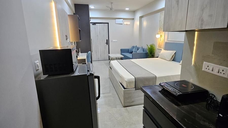 A view from the kitchen to the bedroom, featuring a counter with kitchen equipment, a fridge, and a bed in sight at Urban Suites by BluSalzz, Jaipur.