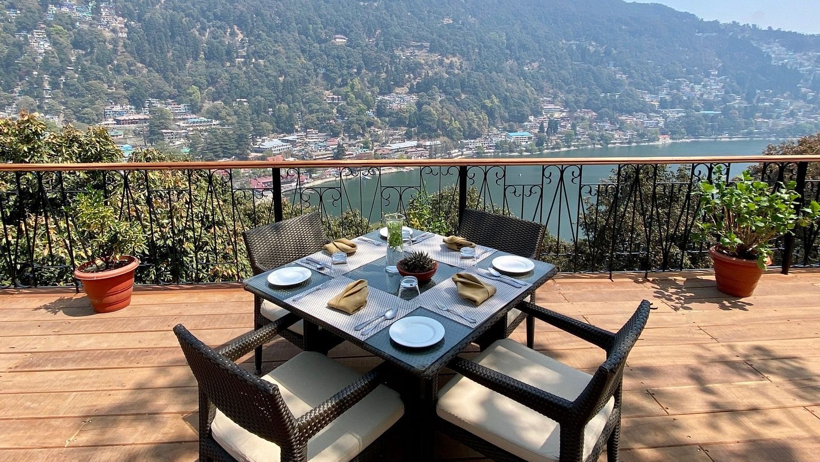 Image showing few chairs placed on the  sides of a square table, pot on either side of the frame, beautifully framed by the backdrop of the mountain ranges.