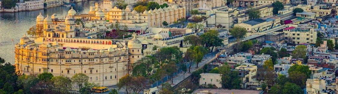 An aerial view of the city of Udaipur with the City Palace, other buildings, a lake and a hill in the background - A must-visit on your 2-Day Udaipur Itinerary.