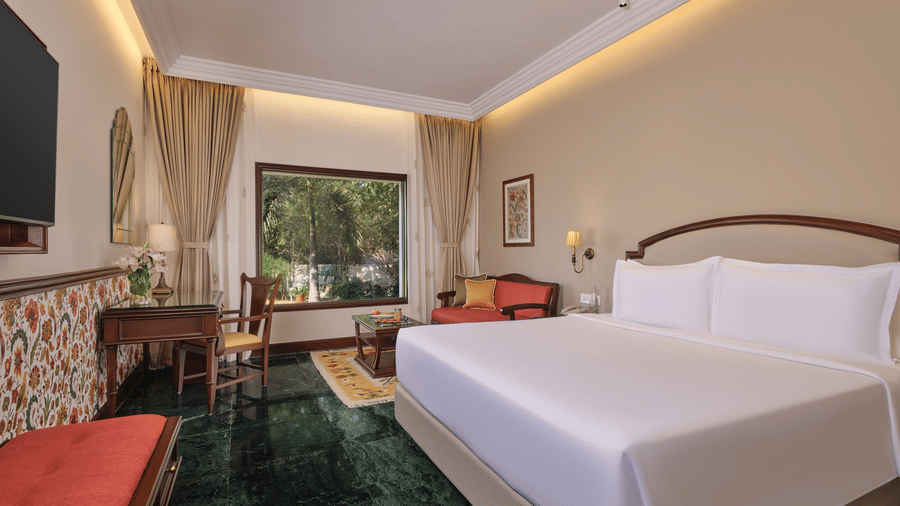The Premium King Garden View Room at The Ummed Ahmedabad featuring a spacious interior with warm lighting and a king size bed facing the TV mounted on the wall